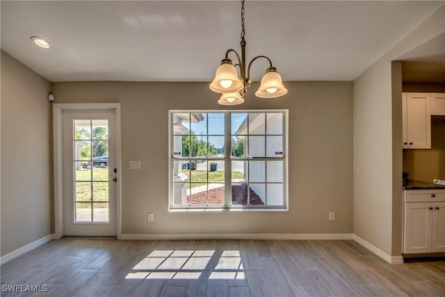 unfurnished dining area featuring light wood-type flooring, an inviting chandelier, baseboards, and recessed lighting