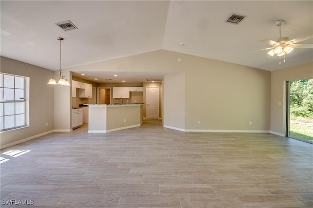 unfurnished living room featuring visible vents, vaulted ceiling, baseboards, and ceiling fan with notable chandelier