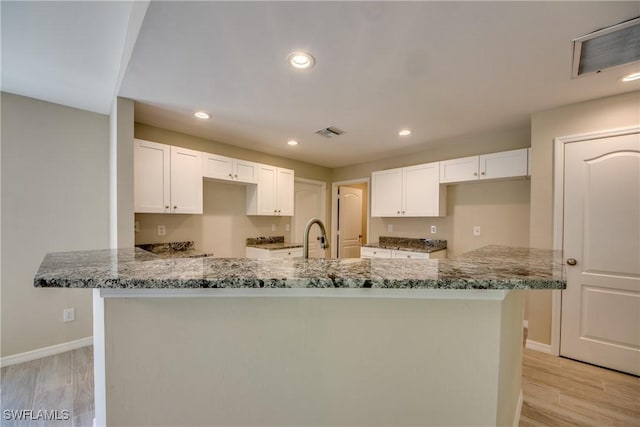 kitchen with stone countertops, visible vents, light wood finished floors, and white cabinetry