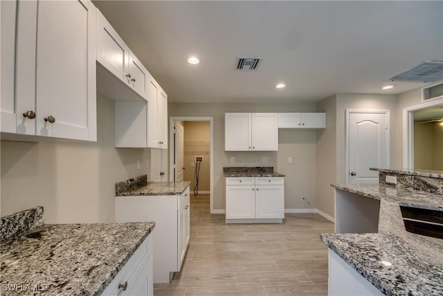 kitchen with white cabinetry, visible vents, and light stone counters