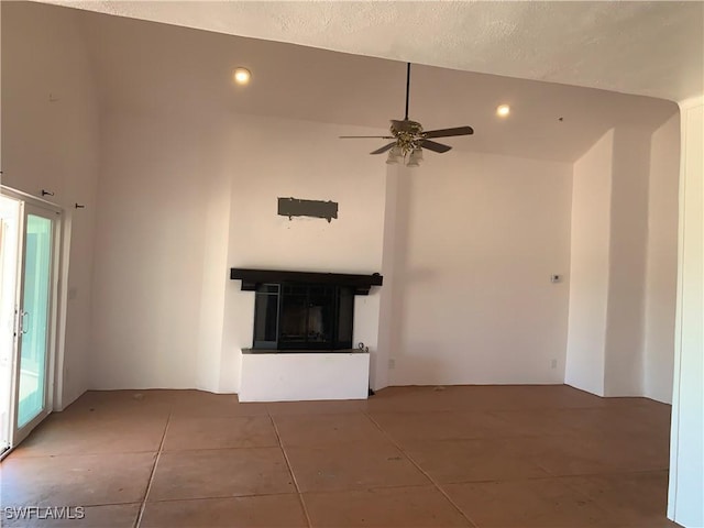 unfurnished living room featuring ceiling fan, tile patterned flooring, recessed lighting, a towering ceiling, and a glass covered fireplace