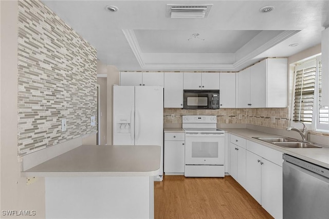 kitchen with white appliances, visible vents, a sink, a tray ceiling, and backsplash