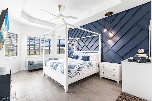 bedroom with a ceiling fan, wood finish floors, and a raised ceiling