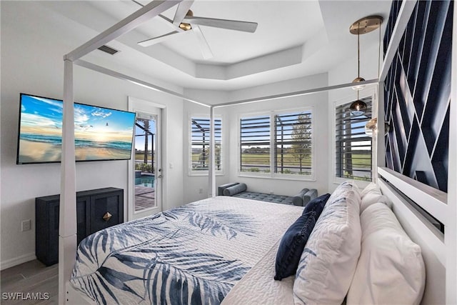 bedroom with wood finished floors, multiple windows, a raised ceiling, and access to exterior