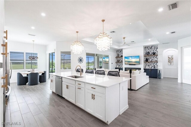 kitchen with a chandelier, a kitchen island with sink, stainless steel dishwasher, white cabinetry, and a sink