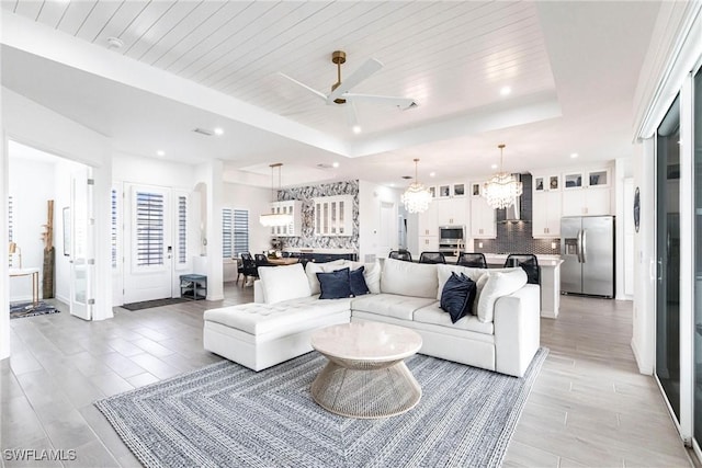 living area featuring ceiling fan with notable chandelier, a tray ceiling, wood ceiling, and recessed lighting