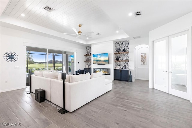 living room featuring baseboards, visible vents, a raised ceiling, a glass covered fireplace, and light wood-type flooring