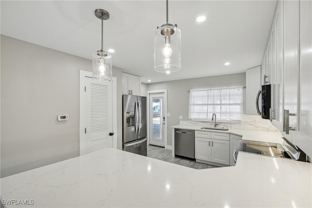 kitchen with appliances with stainless steel finishes, white cabinetry, a sink, and light stone counters