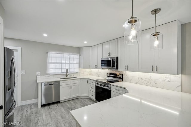 kitchen with light stone counters, stainless steel appliances, light wood-style flooring, decorative backsplash, and a sink