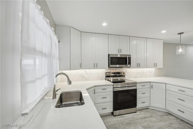 kitchen featuring light wood-style flooring, stainless steel appliances, light countertops, white cabinetry, and a sink