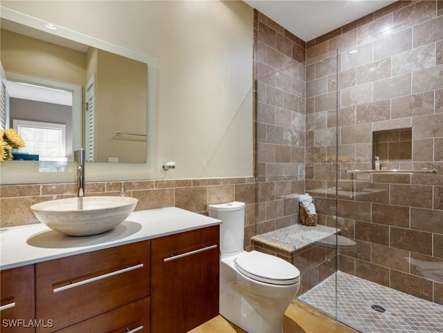 full bathroom with vanity, a tile shower, toilet, and tile walls