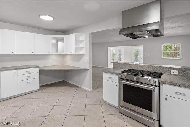 kitchen with light tile patterned floors, open shelves, white cabinetry, wall chimney range hood, and stainless steel gas range oven