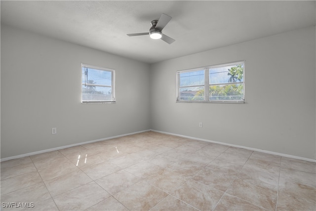 empty room with a ceiling fan, light tile patterned flooring, and baseboards