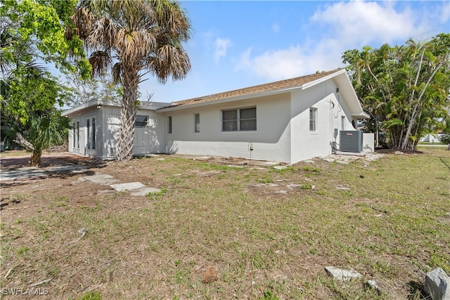 back of property with central air condition unit, a lawn, and stucco siding