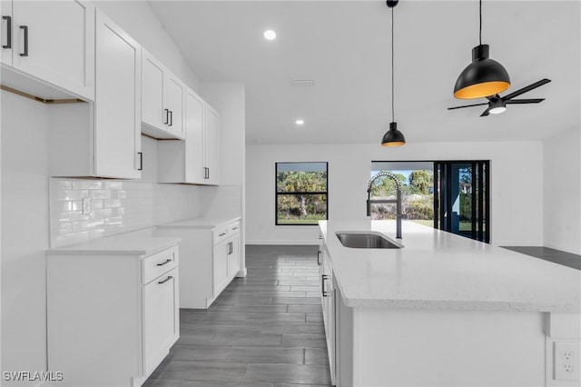 kitchen with light stone counters, a sink, white cabinetry, decorative backsplash, and a center island with sink