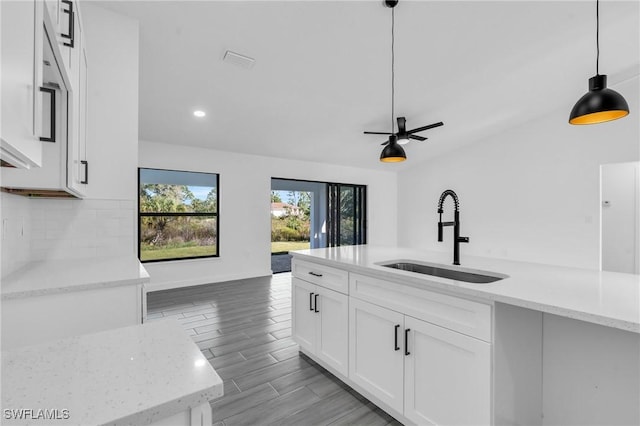 kitchen featuring decorative light fixtures, tasteful backsplash, white cabinets, a sink, and light stone countertops