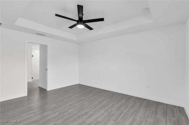 spare room featuring baseboards, visible vents, a raised ceiling, ceiling fan, and wood finish floors