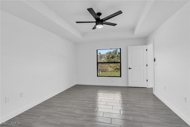 empty room featuring baseboards, a tray ceiling, a ceiling fan, and wood tiled floor