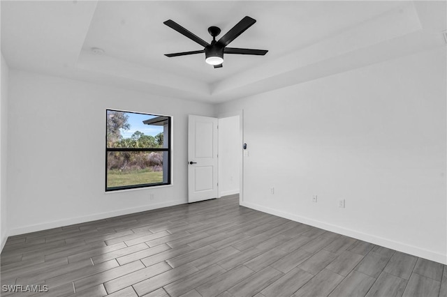 empty room with a tray ceiling, ceiling fan, baseboards, and wood finished floors