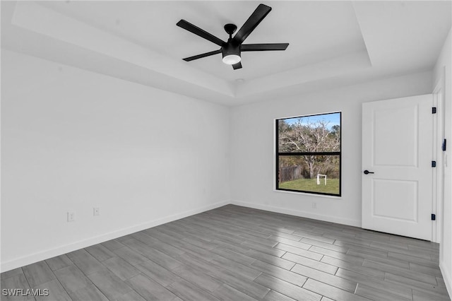 empty room featuring wood tiled floor, baseboards, and a raised ceiling