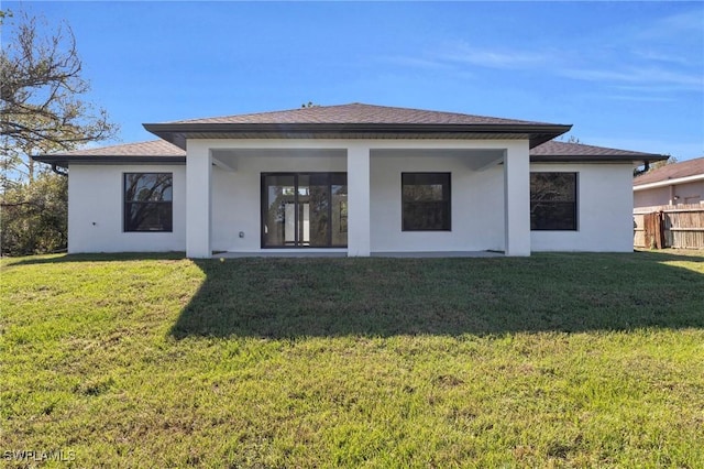 rear view of house with fence, a lawn, and stucco siding