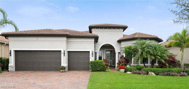 mediterranean / spanish house featuring a garage, decorative driveway, a front yard, and stucco siding