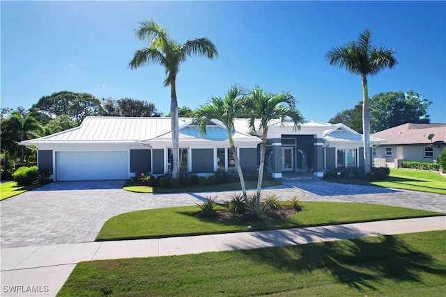 single story home featuring decorative driveway, metal roof, an attached garage, and a front lawn