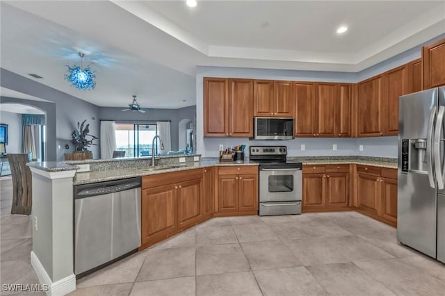 kitchen featuring arched walkways, brown cabinets, stainless steel appliances, a sink, and a peninsula