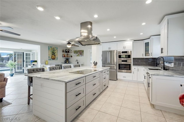 kitchen featuring stainless steel appliances, decorative backsplash, a sink, ceiling fan, and island range hood