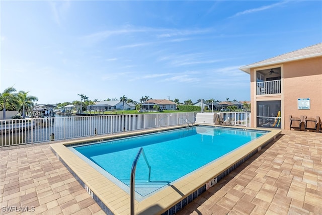 pool with a patio area, fence, and a water view