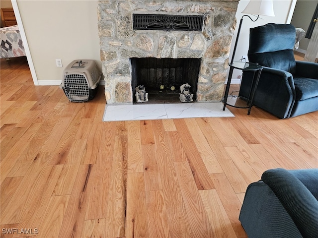 living room with a stone fireplace, baseboards, and wood finished floors