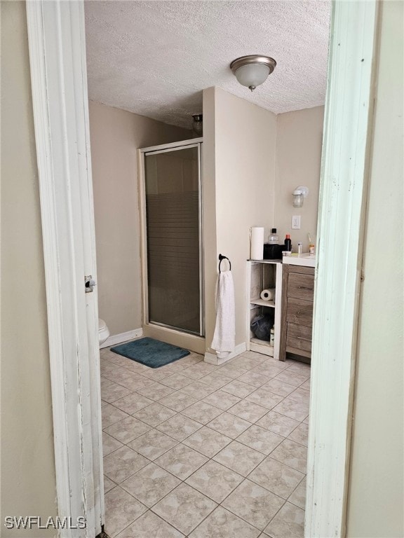 full bathroom with tile patterned flooring, a shower stall, toilet, vanity, and a textured ceiling