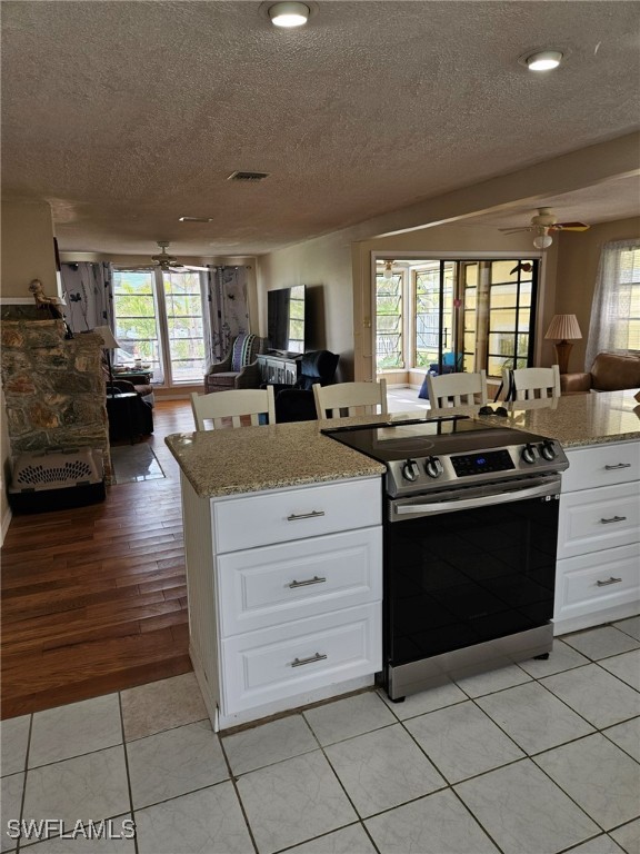 kitchen featuring open floor plan, visible vents, stainless steel range with electric stovetop, and ceiling fan