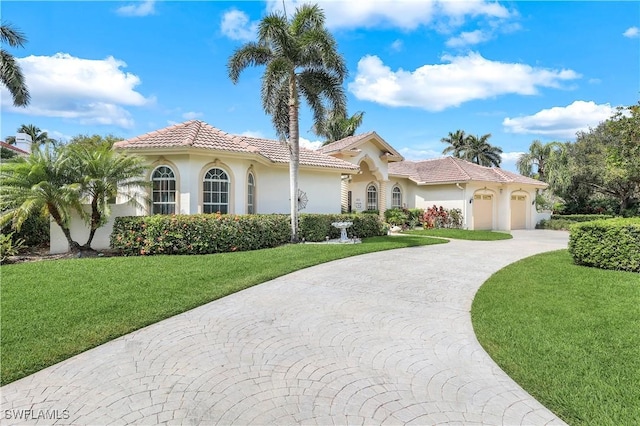 mediterranean / spanish house featuring an attached garage, stucco siding, a front yard, curved driveway, and a tiled roof