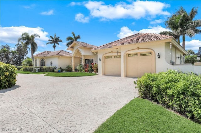 mediterranean / spanish-style home featuring an attached garage, a tile roof, curved driveway, and stucco siding