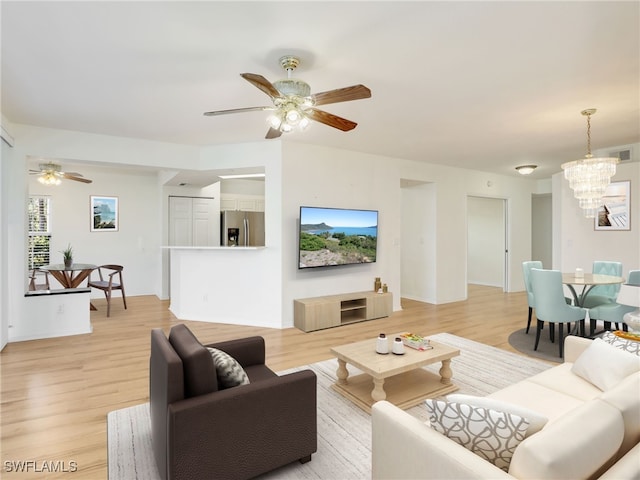 living area featuring ceiling fan with notable chandelier, light wood finished floors, and visible vents