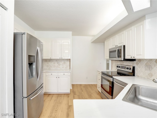 kitchen featuring light wood-type flooring, white cabinets, stainless steel appliances, and a sink