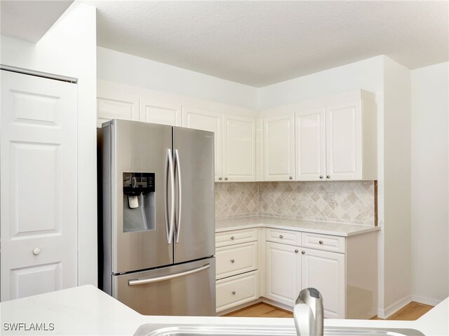 kitchen featuring light wood-style flooring, white cabinets, light countertops, stainless steel fridge with ice dispenser, and tasteful backsplash