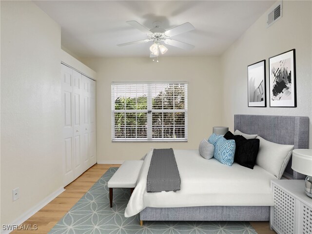 bedroom featuring ceiling fan, wood finished floors, visible vents, baseboards, and a closet