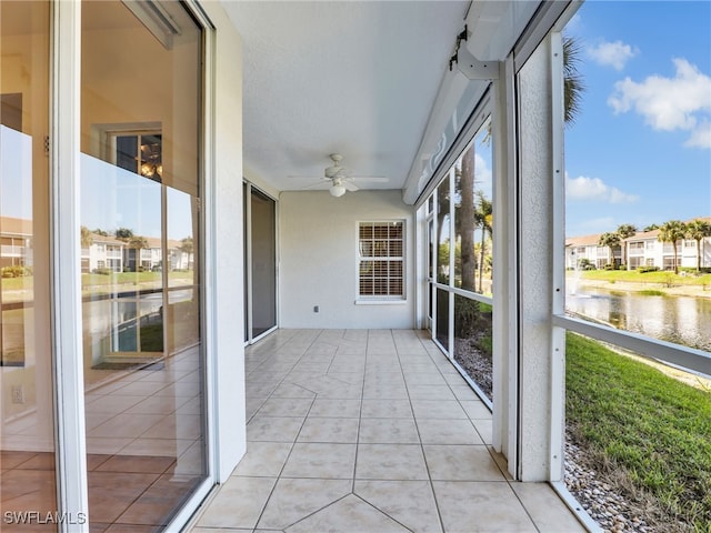 unfurnished sunroom featuring a water view, a residential view, and a ceiling fan