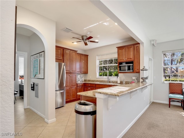 kitchen featuring visible vents, brown cabinetry, freestanding refrigerator, a peninsula, and a kitchen bar