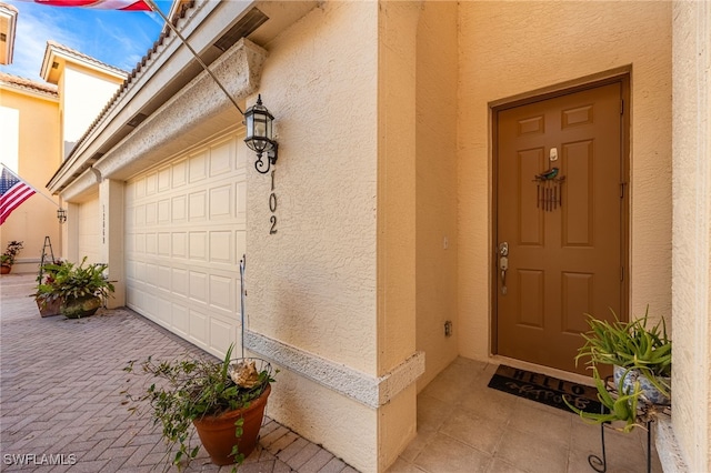 view of exterior entry with an attached garage, stucco siding, and decorative driveway