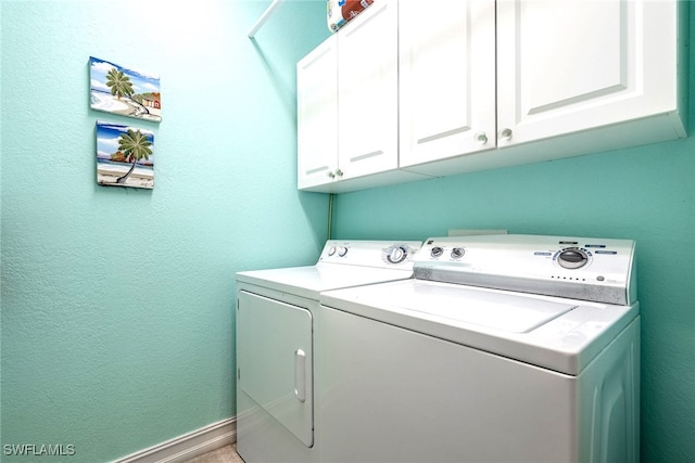 clothes washing area featuring a textured wall, cabinet space, and washer and dryer