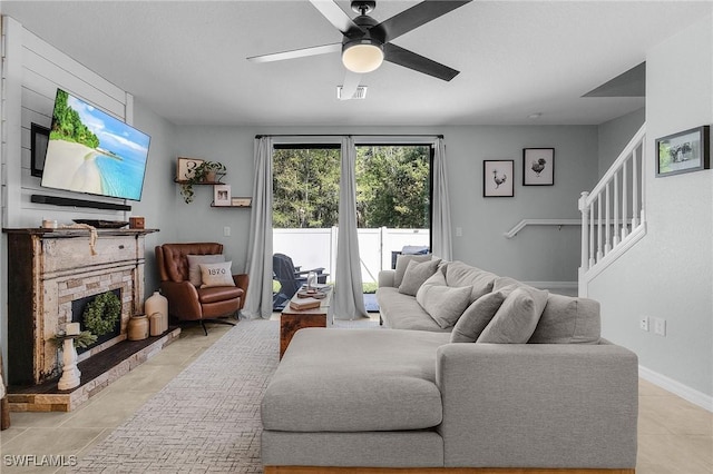 living area with light tile patterned floors, a ceiling fan, visible vents, baseboards, and a stone fireplace