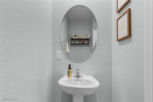 bathroom with a sink, visible vents, and a textured wall