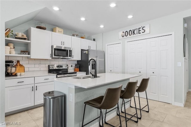 kitchen featuring open shelves, a kitchen island with sink, a sink, stainless steel appliances, and tasteful backsplash