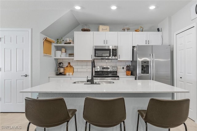 kitchen with a kitchen bar, a sink, backsplash, appliances with stainless steel finishes, and white cabinets