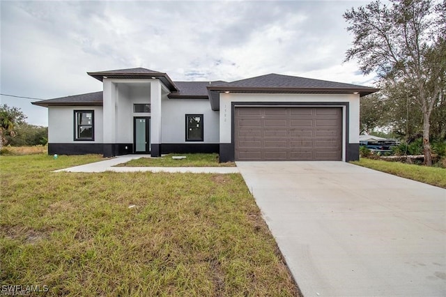 prairie-style home with an attached garage, driveway, a front yard, and stucco siding