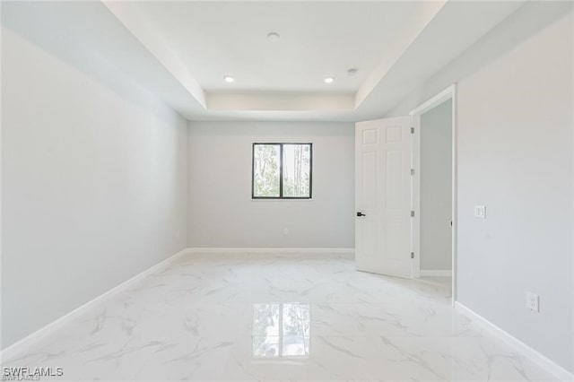 spare room with a tray ceiling, marble finish floor, and baseboards