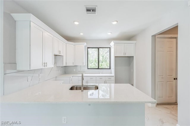 kitchen with light stone counters, white cabinets, visible vents, and a sink